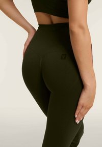 Korkeavyötäröiset, tummanvihreät leggingsit joustavasta kankaasta, joissa on sileä pinta ja pieni logotyyppinen yksityiskohta takana.