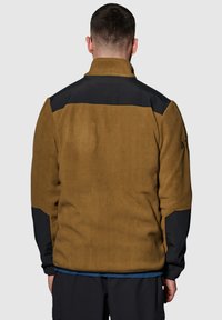 Bruine fleecejack met zwarte accentpanelen, hoge kraag en een zachte textuur. Heeft een ontspannen pasvorm en elastische manchetten.