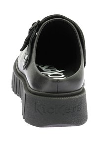 Scarpe in pelle nera con retro tondo, suola spessa e testurizzata, e una chiusura laterale. Il marchio è impresso sul tallone.