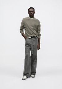 Lysegrå ribstrikket sweater, lagdelt over en hvid T-shirt. Grå jeans med vide ben og bindebånd foran. Hvide og grå sneakers.