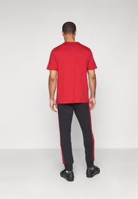 T-shirt de algodão vermelha combinada com calças de moletom pretas com riscas laterais vermelhas. Modelo de costas, usando calçado preto.