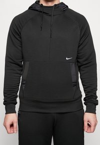 Czarna bluza Nike z teksturowanej tkaniny, dopasowany krój, kaptur ze sznurkiem, kieszeń kangurza oraz biały detal z logo na klatce piersiowej.