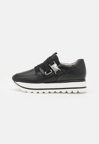 Sneaker en cuir noir avec des bandes élastiques et des accents en métal, dotée d'une semelle blanche rembourrée avec des segments arrondis et un design élégant et aérodynamique.