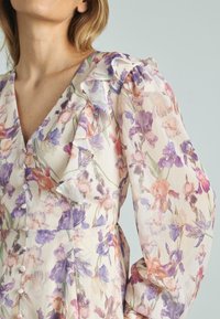 Vestido de estampado floral en tela ligera; cuenta con mangas con volantes, cierre de botones y una mezcla de tonos púrpura, rosa y crema.