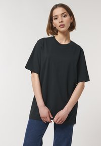 T-shirt en coton noir avec une coupe décontractée, des manches courtes et un col rond. Porté avec un pantalon en denim bleu, sans motifs ni accents visibles.
