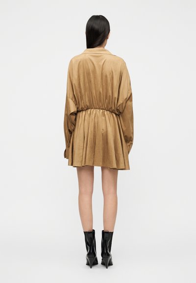 Μπεζ φόρεμα σε στυλ πουκάμισου με μακριά μανίκια, σούρα στη μέση, ρέον φόρεμα και λείο ύφασμα. Συνδυασμένο με γυαλιστερά μαύρα μποτάκια αστραγάλου.