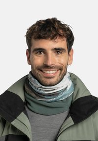 Cuello de multicolores hecho de tela elástica que presenta patrones abstractos. Se lleva sobre una camiseta gris y una chaqueta verde con un acento negro.