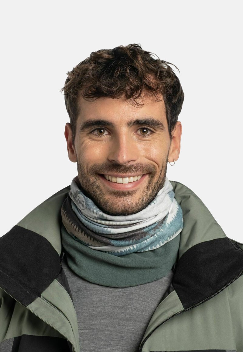 Cuello de multicolores hecho de tela elástica que presenta patrones abstractos. Se lleva sobre una camiseta gris y una chaqueta verde con un acento negro.