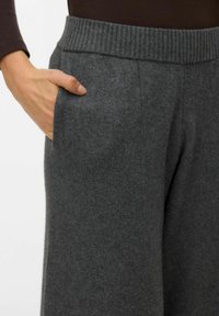Pantalon gris en mélange de laine avec une ceinture élastique côtelée et des poches latérales, présentant une texture douce et une coupe droite.