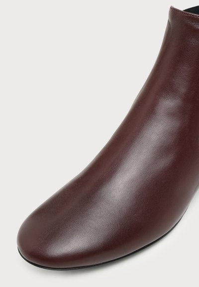 Bottine en cuir marron foncé à texture lisse et bout arrondi, présentée sur un fond clair.