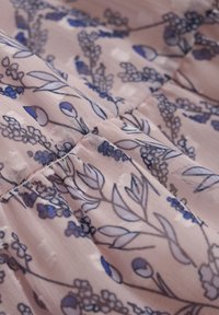 Ljust rosa tyg med blommönster i blått och mörkgrönt, med en texturerad yta och rynkade detaljer längs sömmen.