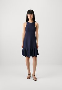 Marinblå ärmlös klänning med en figurnära bodice och en utsvängd, volangad nederdel. Tyget ser slätt ut och är något texturerat.
