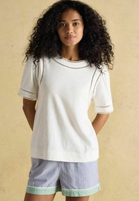 Valgete õhukeste varrukatega kudum, millel on tekstuuriga võrkpaneelid õlgadel. Koos siniste ja valgete triibuliste lühikesed pükstega, rohelise äärega.