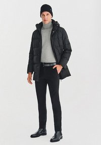 Czarna kurtka puchowa z kapturem, szary sweter z golfem, czarny pasek, czarne spodnie i czarne botki typu chelsea; teksturowany i dopasowany krój.