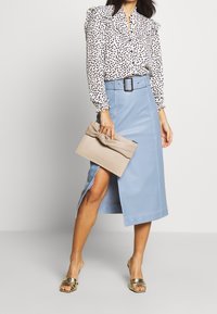 Weiße Bluse mit schwarzen Polka-Dots, Rüschenkragen; hellblauer Lederminirock mit Schlitz; beiger Clutch mit Knoten; goldene Riemchensandalen.