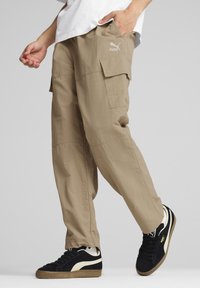 Beige cargobroek met zijzakken, gemaakt van lichte stof, gecombineerd met zwarte sneakers met crèmekleurige accenten en een gestructureerde rubberen zool.
