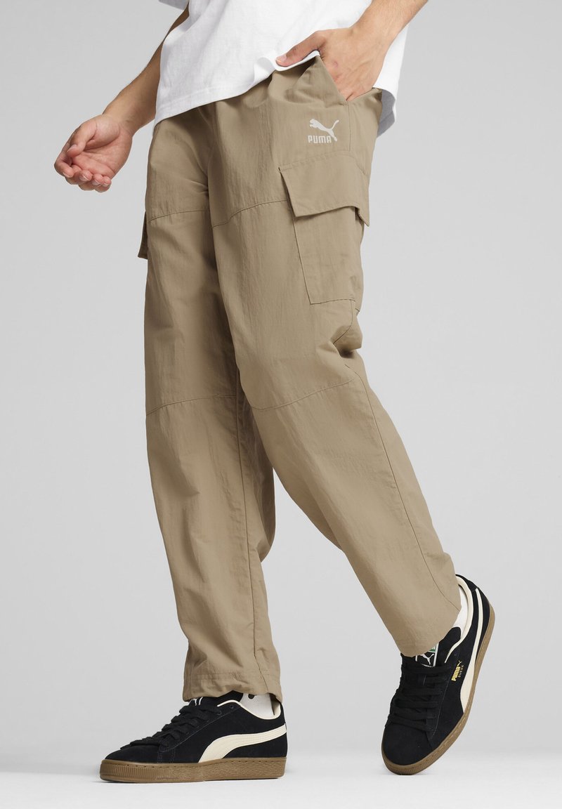 Beige cargobroek met zijzakken, gemaakt van lichte stof, gecombineerd met zwarte sneakers met crèmekleurige accenten en een gestructureerde rubberen zool.