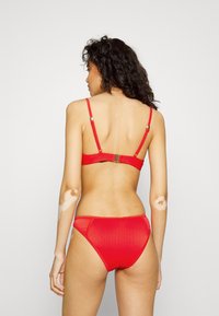 Conjunto de bikini vermelho com textura canelada, alças ajustáveis e fecho de clap em nas costas. Parte de baixo de cintura alta com acabamento liso.