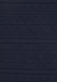 Dunkelblauer, strukturierten Stoff mit geometrischen Mustern aus Dreiecken und Rauten, wobei hervorgehobene Nähte eine taktile Oberfläche schaffen.