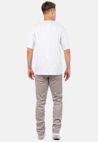 T-shirt blanche à manches courtes avec un col ras du cou, associé à un pantalon en velours côtelé gris clair. Le pantalon présente de discrètes rayures verticales et une coupe slim.