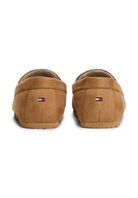 Pantofole in suede marrone con fodera interna morbida. Presentano un piccolo logo ricamato in rosso, bianco e blu sul retro. Suola piatta.