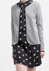 Abito nero con stampe paisley e floreali bianche, sovrapposto a un cardigan grigio texturizzato con motivo a nido d'ape e rifiniture nere.