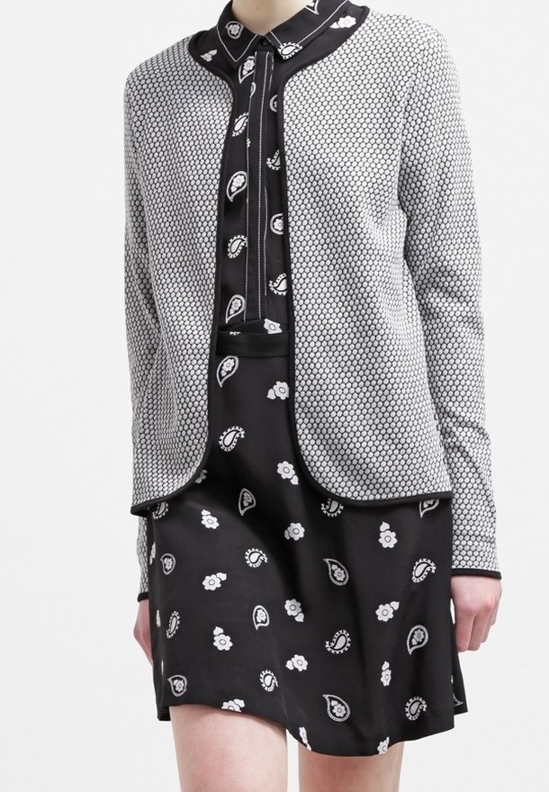 Abito nero con stampe paisley e floreali bianche, sovrapposto a un cardigan grigio texturizzato con motivo a nido d'ape e rifiniture nere.