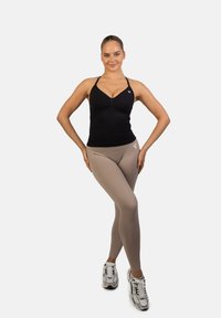 Zwarte fitness tanktop en beige leggings gedragen met witte sneakers. De tanktop heeft dunne bandjes en een aansluitend ontwerp. De leggings zijn glad en rekbaar.