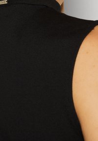 Haut noir sans manches avec une texture lisse et mate, orné d'un subtil accent doré au niveau de l'encolure arrière. Lignes épurées et coupe ajustée.