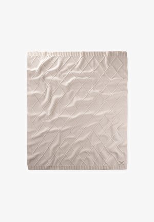 Kremowy dziergany koc z diamentowym wzorem i prążkowanymi krawędziami, rozłożony płasko z drobnymi zagnieceniami i małą metką w rogu.