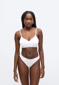 Biele bavlnené braletové podprsenka a tangá sada s výstrihom do V a elastickým pásom s logom "TOMMY HILFIGER" v čiernej a červenej farbe.