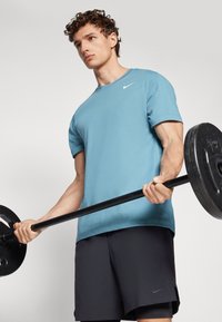 Light blue short-sleeve Nike shirt, black shorts, holding a barbell. Cotton fabric, relaxed fit, with prominent logo on the chest.