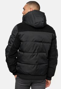 Sort pufferjakke med hætte, der har paneldetaljer, ribbede elementer på skuldrene og en tekstureret overflade. Kviltet design for varme.