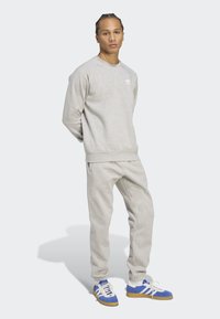 Svetlošedá mikina s rebrovanými manžetami, zodpovedajúce tepláky a modré tenisky s bielymi pruhmi. Jednoduchý dizajn, voľný strih, mäkká textúra.