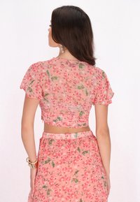 Lyserød blomstercrop top med korte ærmer, der har en gennemsigtig tekstur og flæsedetaljer. Koordinerende blomsterskirt med elastisk talje.
