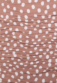 Zgniatana tkanina w kolorze terakoty, z nieregularnymi białymi kropeczkami. Struktura wydaje się miękka i zgromadzona w poziome linie.
