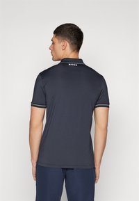 Μπλουζάκι πόλο ναυτικού χρώματος με κοντά μανίκια, διακριτικές λευκές λεπτομέρειες στον γιακά και τα μανίκια, και λογότυπο BOSS στο πίσω μέρος του λαιμού. Απαλή υφή.