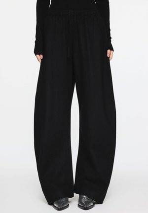 Schwarze Weitbein-Hose mit elastischem Bund und Kordelzug. Weicher Stoff mit glatter Textur, mit seitlichen Nahtdetails.