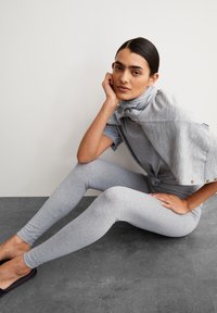 Gray fitted leggings with a smooth texture, paired with a short, knotted gray top featuring shoulder accents and a high neck.
