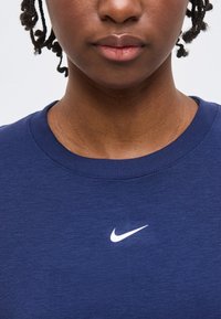 Κλείσιμο ενός ατόμου που φοράει μπλε μπλουζάκι Nike με λευκό λογότυπο Swoosh στο κέντρο του λαιμού.