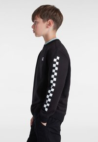 Sudadera negra con un cuello azul claro, que presenta un patrón de cuadros en la manga izquierda y un logotipo en el pecho.