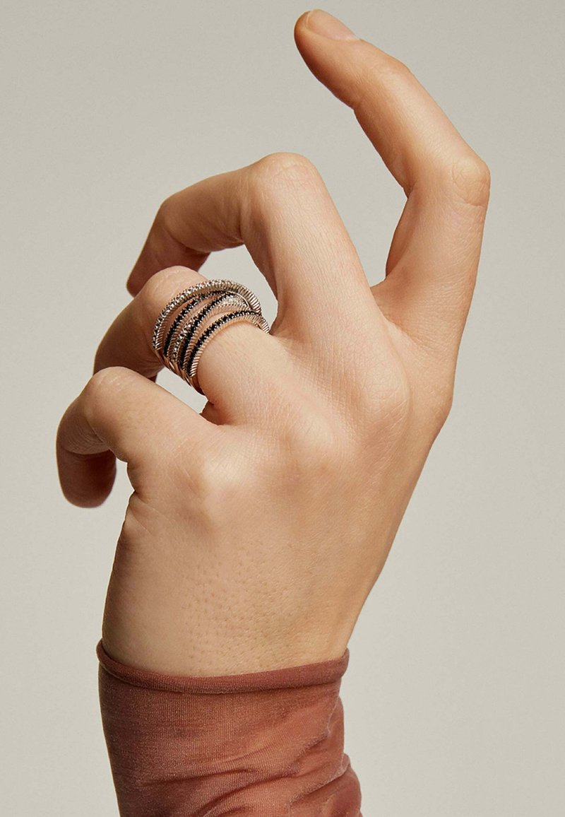 Conjunto de anillos de plata con múltiples bandas, que presentan superficies texturizadas y lisas, llevados en una mano con la palma hacia arriba. Se ve una suave funda de tela.