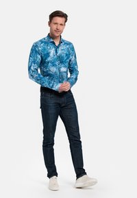 Blauwe langemouwen shirt met een palmenbladpatroon, gecombineerd met donkere jeans en witte sneakers. Glad materiaal met een getailleerd ontwerp.