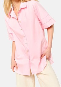 Light pink short-sleeve button-up shirt made of smooth fabric, featuring a classic collar and subtle design lines on sleeves.