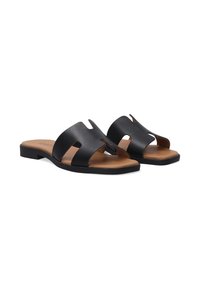 Schwarze Leder-Sandalen zum Hineinschlüpfen mit ausgeschnittenem Design, flacher Sohle und braunem Fußbett, die eine schlichte und moderne Form aufweisen.