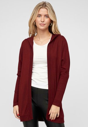 Mørkerød hættetrøje i cardigan-stil med ribbestrikkede ærmer og kant, åben frontdesign, båret over en hvid top og sorte bukser, minimal tekstur.