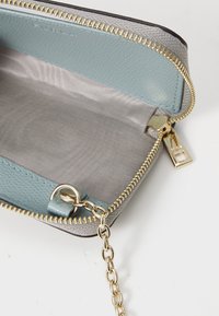 Gray leather wallet with a light blue interior, gold zipper, chain strap, and a textured surface. Features a keyring attachment inside.
