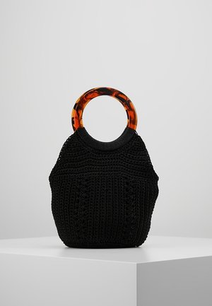 Sort strikket håndtaske med runde håndtag i plastik med skildpaddeskalsmønster, vist på en hvid piedestal mod en grå baggrund.