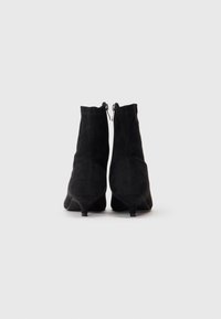 Stivaletti neri in suede con una forma affusolata, dotati di un piccolo tacco kitten e di una chiusura con zip sul retro. Texture liscia, senza motivi visibili.