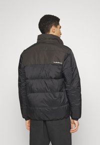 Puffer jacket in black with a contrasting brown upper section, featuring a high collar and elasticized cuffs. Logo on the back.